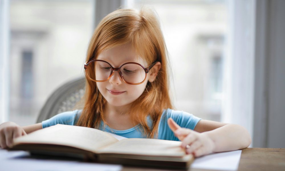 Une élève à lunettes lit un livre à haute voix devant un public.