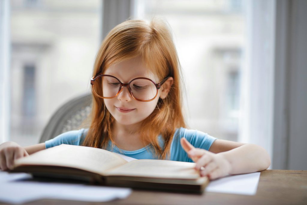 Une élève à lunettes lit un livre à haute voix devant un public.