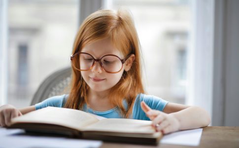 Une élève à lunettes lit un livre à haute voix devant un public.