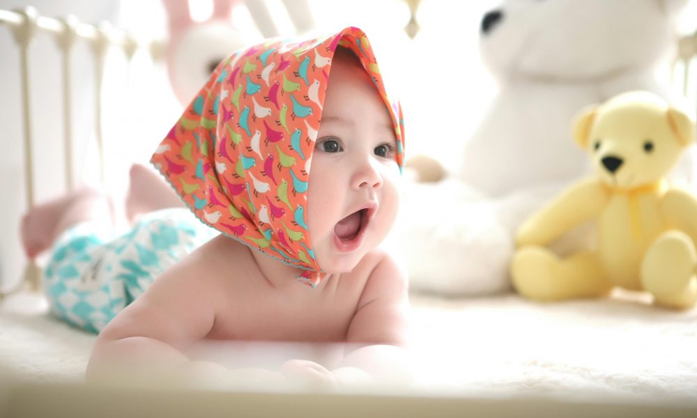 Un adorable bébé dans son parc et avec un foulard sur la tête.