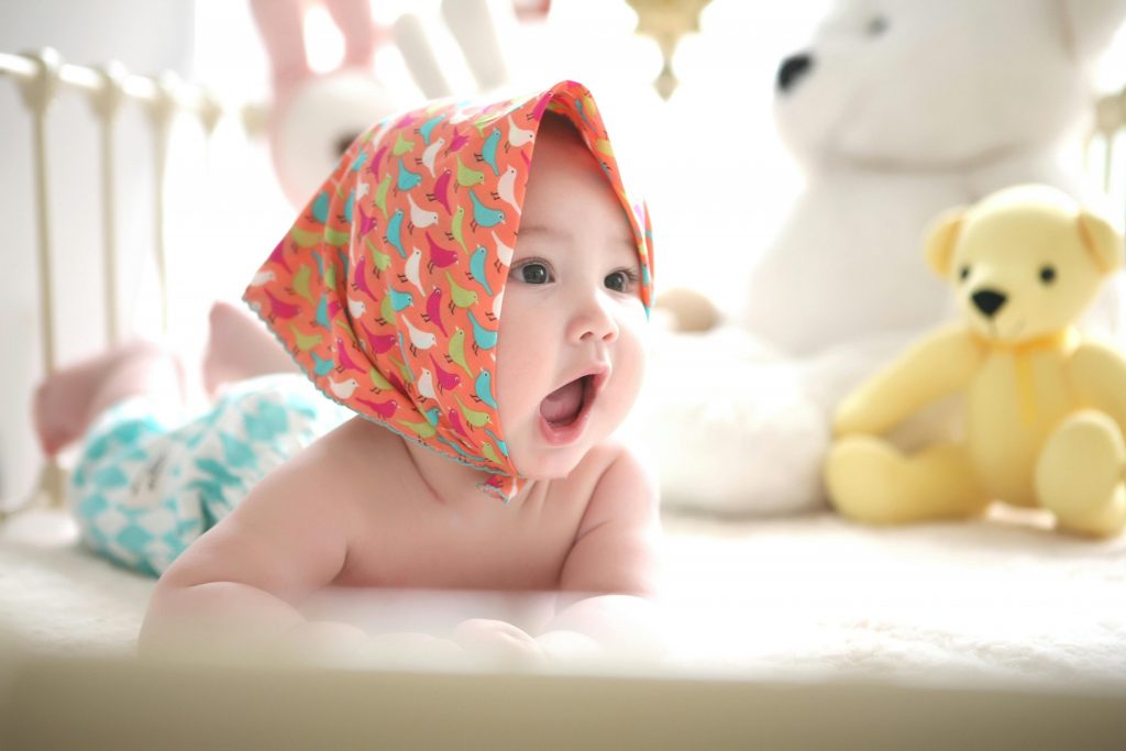 Un adorable bébé dans son parc et avec un foulard sur la tête.