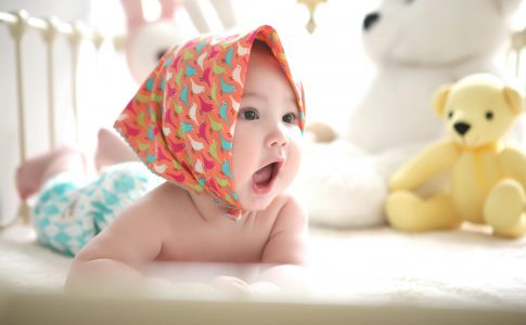 Un adorable bébé dans son parc et avec un foulard sur la tête.