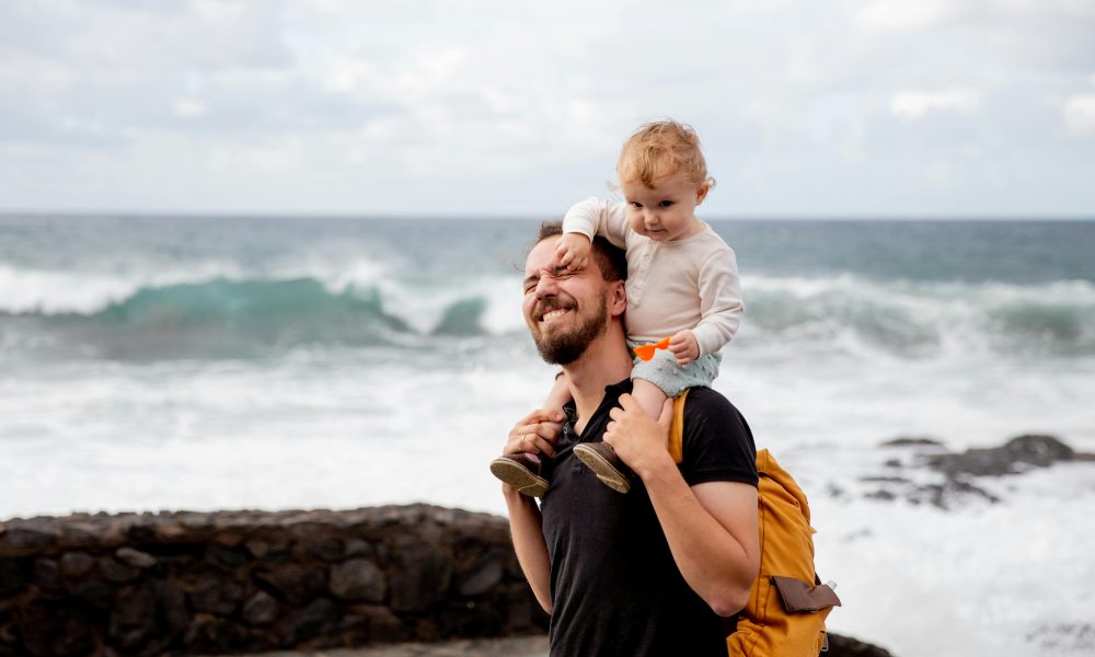 Un père portant son enfant sur les épaules, passant un moment de complicité à la plage.