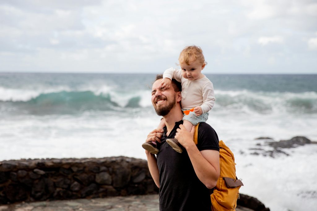 Un père portant son enfant sur les épaules, passant un moment de complicité à la plage.