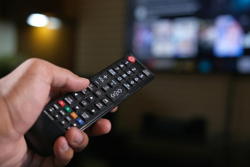 Une personne tenant une télécommande pointée vers la télévision connectée à un service de streaming.