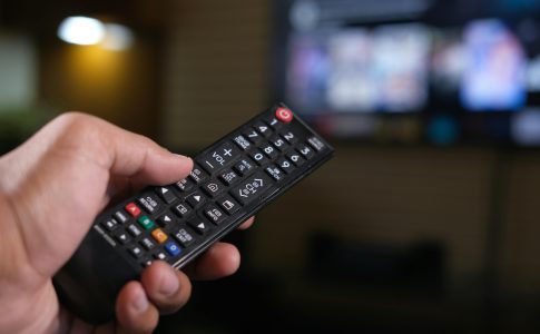 Une personne tenant une télécommande pointée vers la télévision connectée à un service de streaming.