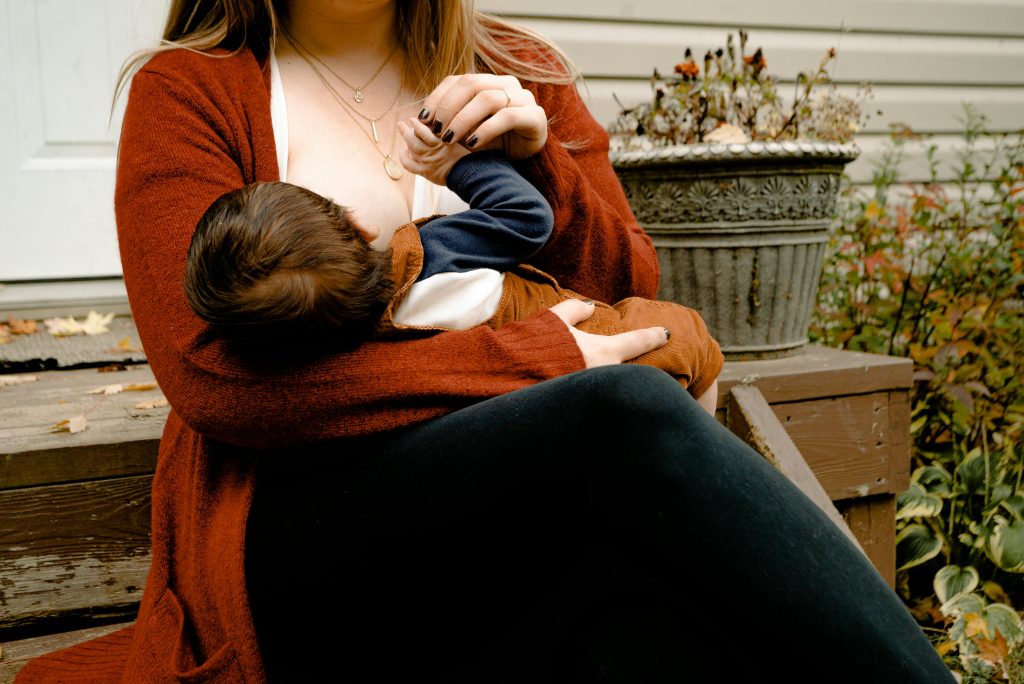 Une mère qui nourrit son bébé au sein, devant le pas-de-porte d’une maison.