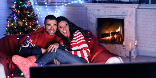 Un couple confortablement installé dans leur salon, regardant un film de Noël à la télévision.