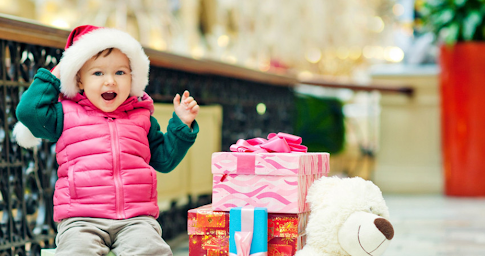 Un enfant souriant à côté de plusieurs cadeaux emballés pour Noël.