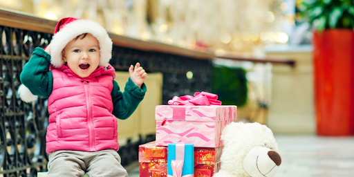 Un enfant souriant à côté de plusieurs cadeaux emballés pour Noël.