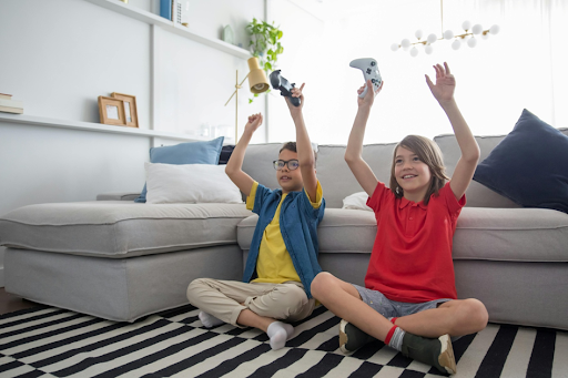 Des jeunes garçons, manettes à la main, assis dans un salon et jouant à un jeu sur console.