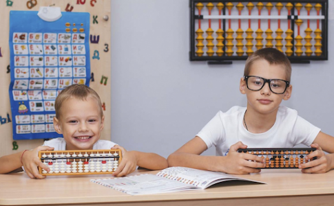 Deux enfants d’âge différents assis à une table d’école et tenant un boulier à compter.