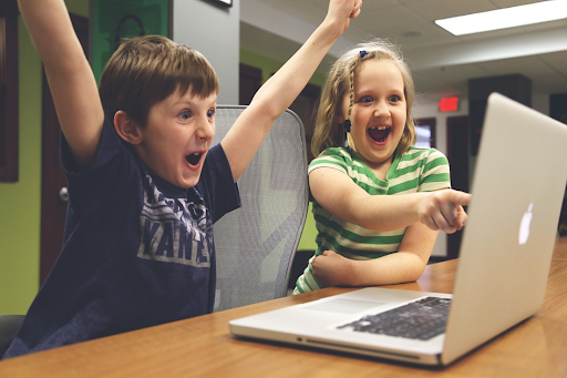 Deux enfants, l’un levant les bras de la victoire, en train de s’amuser devant un ordinateur portable.