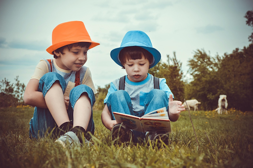 Deux jeunes garçons en train de lire un livre dans une prairie, assis à même l’herbe.