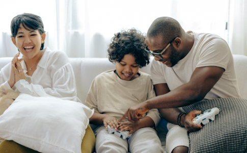 Un enfant jouant à un jeu vidéo de console avec ses parents, dans leur salon.