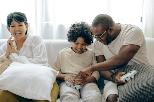 Un enfant jouant à un jeu vidéo de console avec ses parents, dans leur salon.