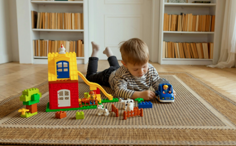Un jeune garçon allongé sur un tapis dans sa chambre, en train de jouer à des jouets multicolores.