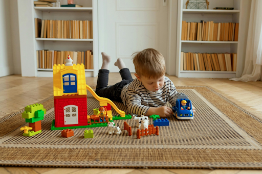 Un jeune garçon allongé sur un tapis dans sa chambre, en train de jouer à des jouets multicolores.