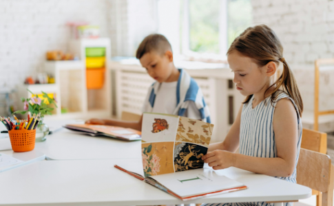 Une fillette assise à son bureau en train de lire avec un jeune garçon assis à ses côtés.