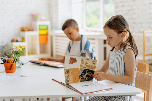 Une fillette assise à son bureau en train de lire avec un jeune garçon assis à ses côtés.
