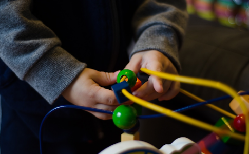Une jeune enfant en train de jouer à un boulier en bois aux couleurs différentes.