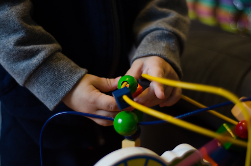 Une jeune enfant en train de jouer à un boulier en bois aux couleurs différentes.
