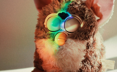 Une peluche Furby posé sur une table et illuminé par un rayon de lumière multicolore.