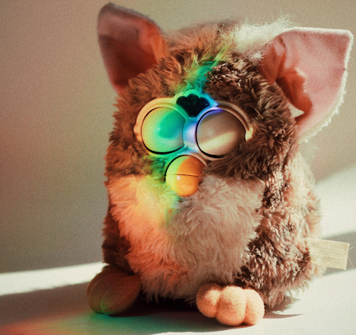 Une peluche Furby posé sur une table et illuminé par un rayon de lumière multicolore.
