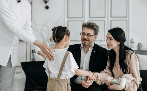 De futurs parents accueillent une petite fille qu’ils vont adopter, avec un responsable des services sociaux à côté.