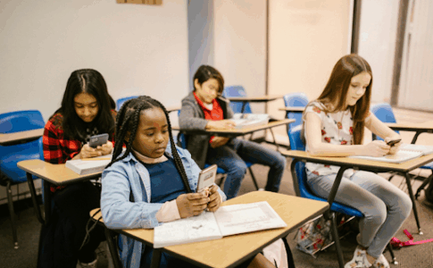 De jeunes élèves assis à leur bureau, en classe, en traine de consulter leur smartphone.