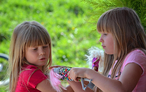 Deux fillettes blondes en train de jouer avec des barbies en plein air.