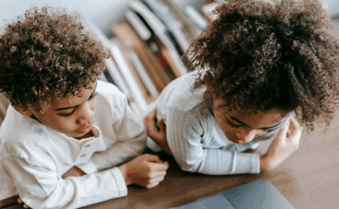 Deux jeunes enfants visionnent un contenu sur un ordinateur portable posé sur un bureau.