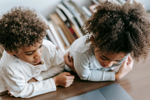 Deux jeunes enfants visionnent un contenu sur un ordinateur portable posé sur un bureau.