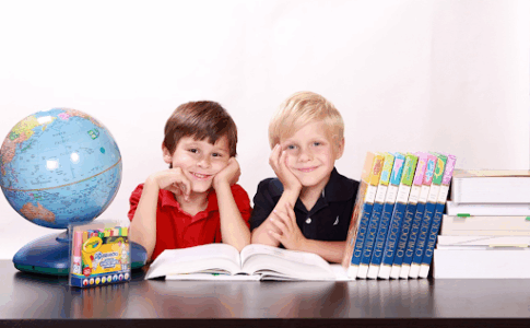 Deux jeunes garçons souriants, assis à une table, avec des ouvrages d’école posés dessus.