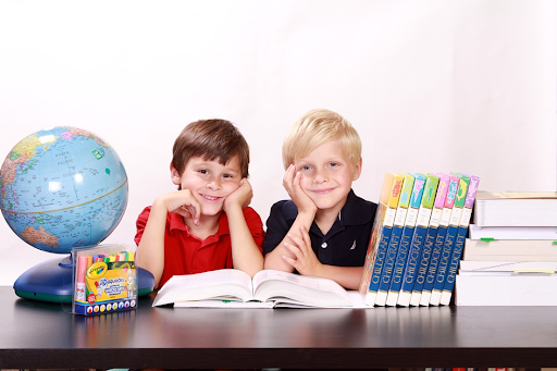 Deux jeunes garçons souriants, assis à une table, avec des ouvrages d’école posés dessus.