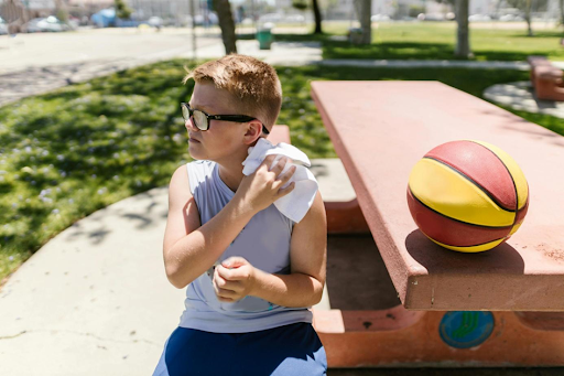 Un garçon assis à un banc, s’essuyant avec une serviette propre, un ballon de basket à côté.