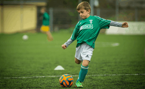 Un jeune garçon en maillot vert qui tape dans un ballon de foot.