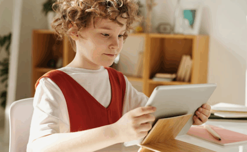 Une enfant assis à son bureau, tenant une tablette numérique dans les mains.