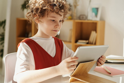 Une enfant assis à son bureau, tenant une tablette numérique dans les mains.