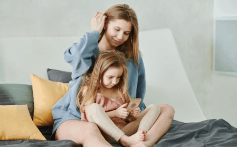 Une mère et sa fille souriantes consultent ensemble un smartphone sur un lit.