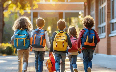 De jeunes élèves portant leurs cartables et marchant vers l’entrée de leur école.