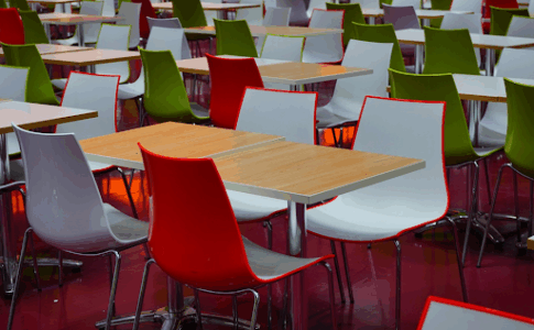 Des tables et des chaises multicolores d’un réfectoire scolaire.