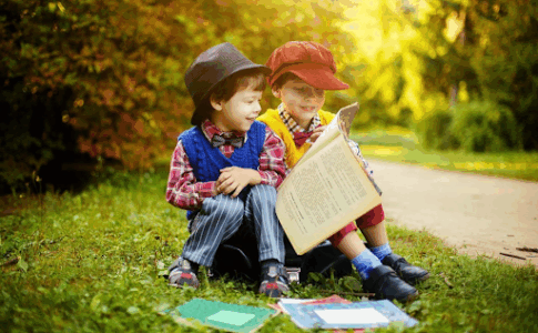 Deux jeunes enfants lisant des livres, assis sur une pelouse près d’une petite allée.