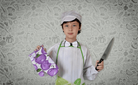 Un jeune garçon en tenue de cuisinier, un couteau à la main et une moufle dans l’autre.