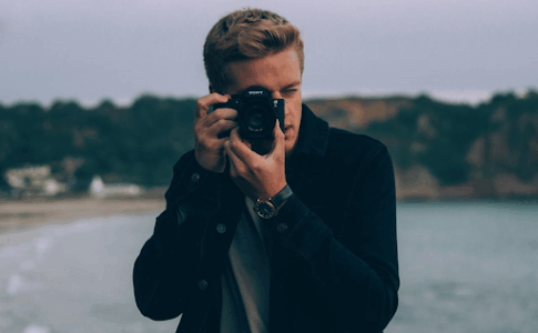 Un jeune homme au bord d’un lac, en pleine prise d’images.