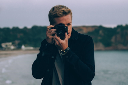 Un jeune homme au bord d’un lac, en pleine prise d’images.