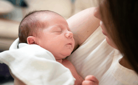 Un petit bébé endormi dans les bras de sa mère.