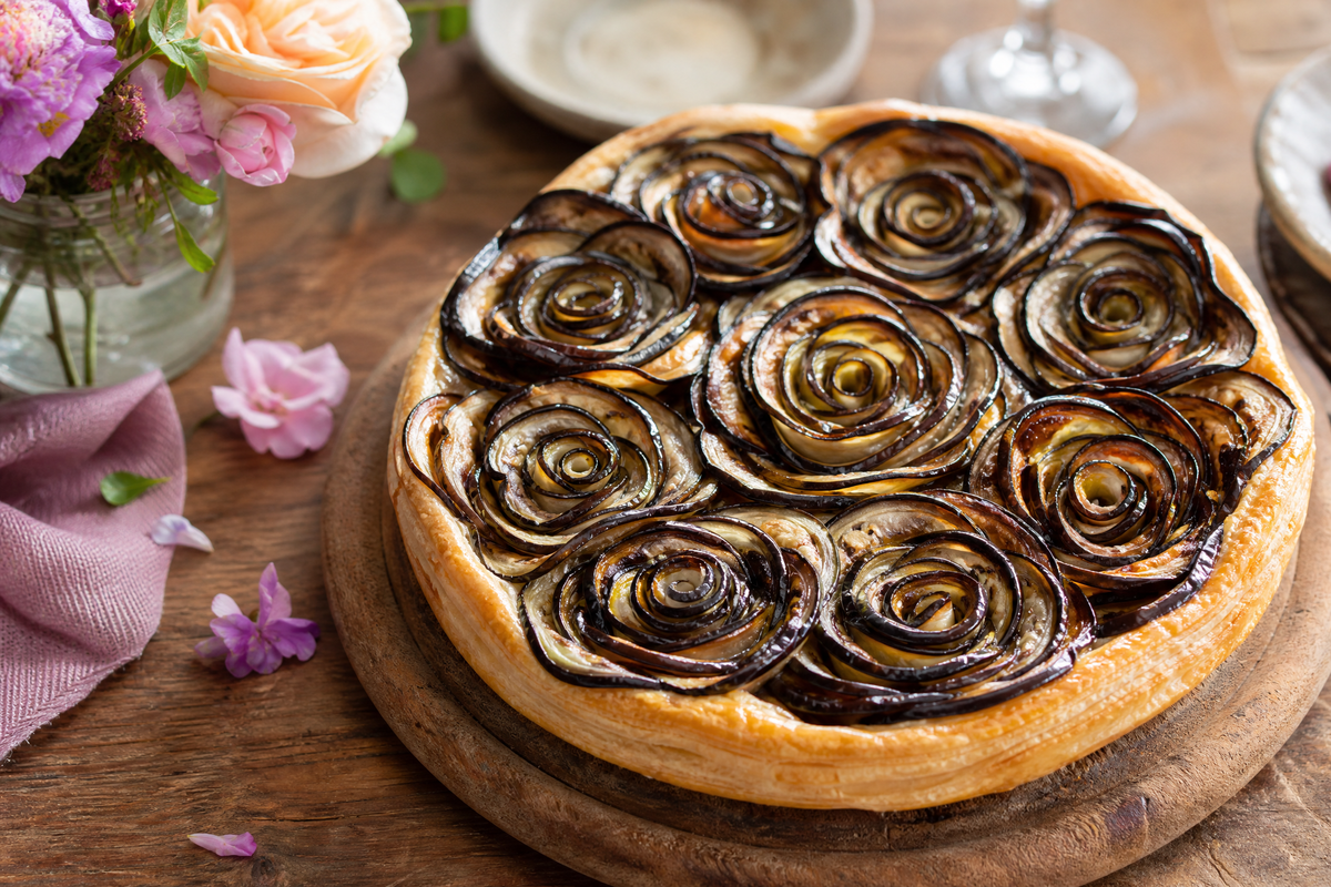 Une tarte salée surmontée de plusieurs rosaces d'aubergines grillées.
