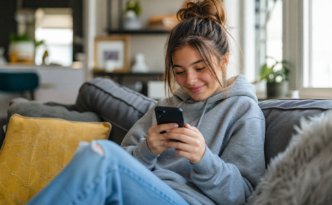 Jeune fille souriante regardant son téléphone portable dans un salon.