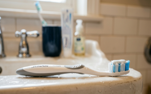 Une brosse à dents posée sur le rebord d'un lavabo de salle de bain avec du dentifrice.